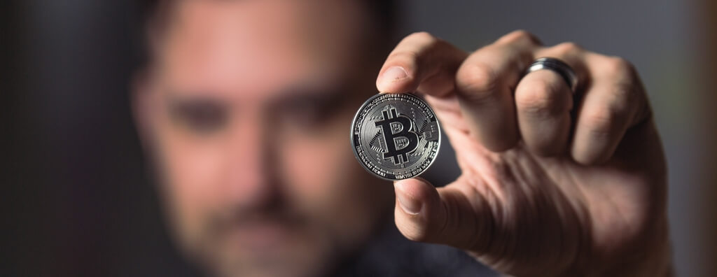 Mann hält einen silbernen Bitcoin